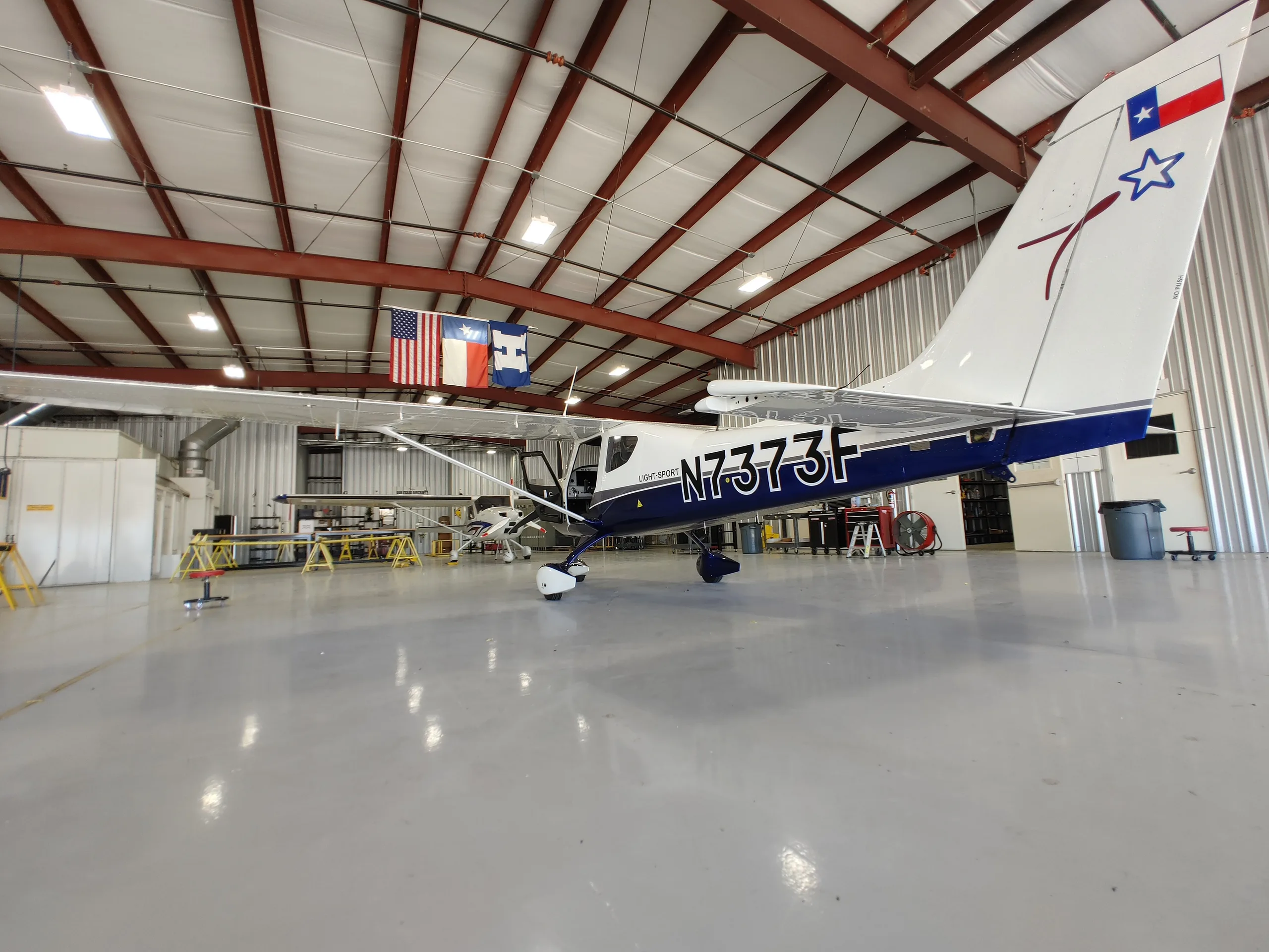 A white and blue Texas Aircraft Colt N7373F parked inside a hangar.