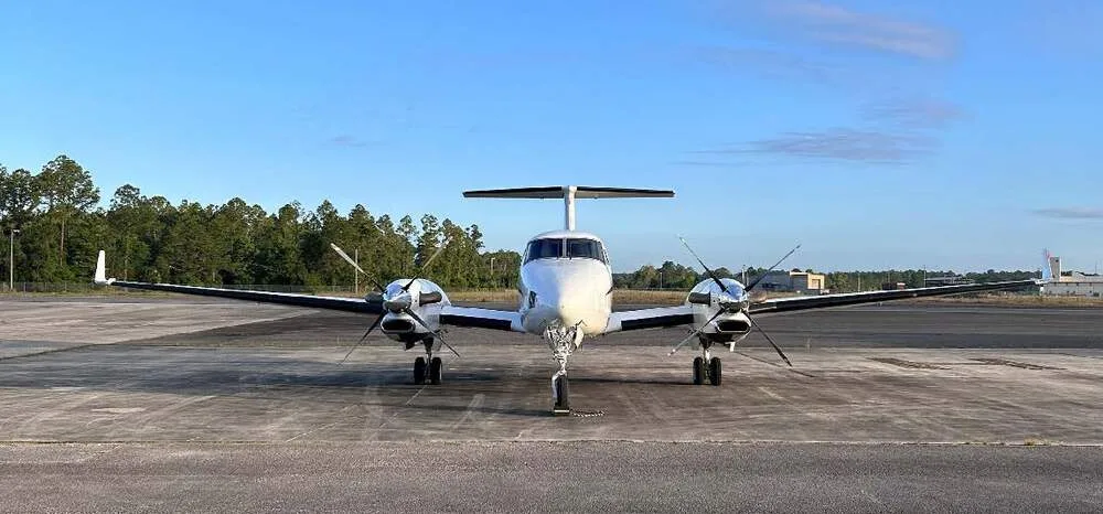 A white Beechcraft King Air 350 turboprop aircraft is viewed head-on, parked on an asphalt tarmac.
