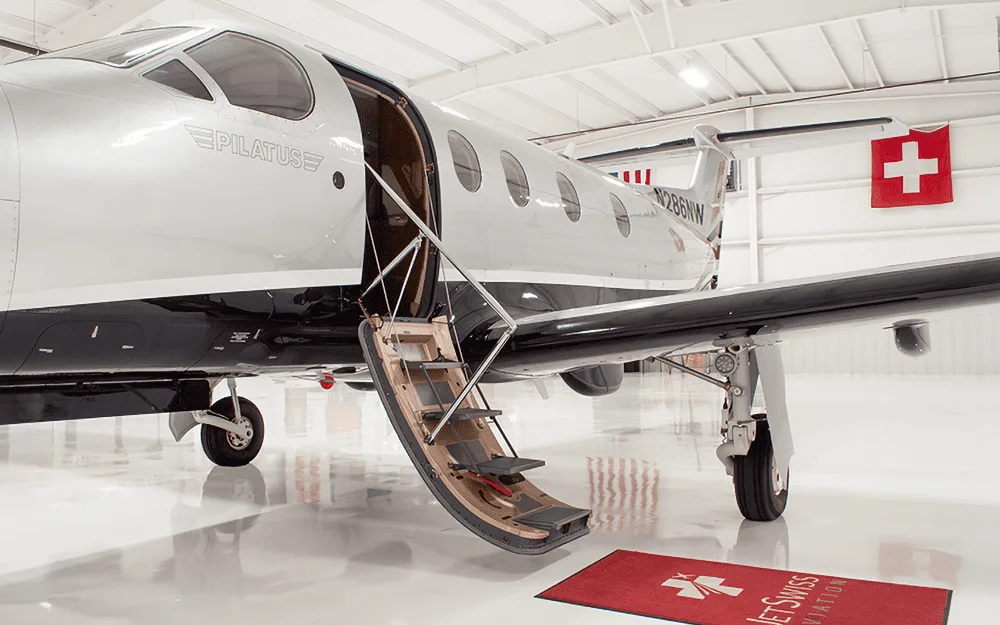 A silver and black Pilatus PC-12 NG aircraft with registration N286NW, parked in a hangar with its passenger door open and stairs extended.