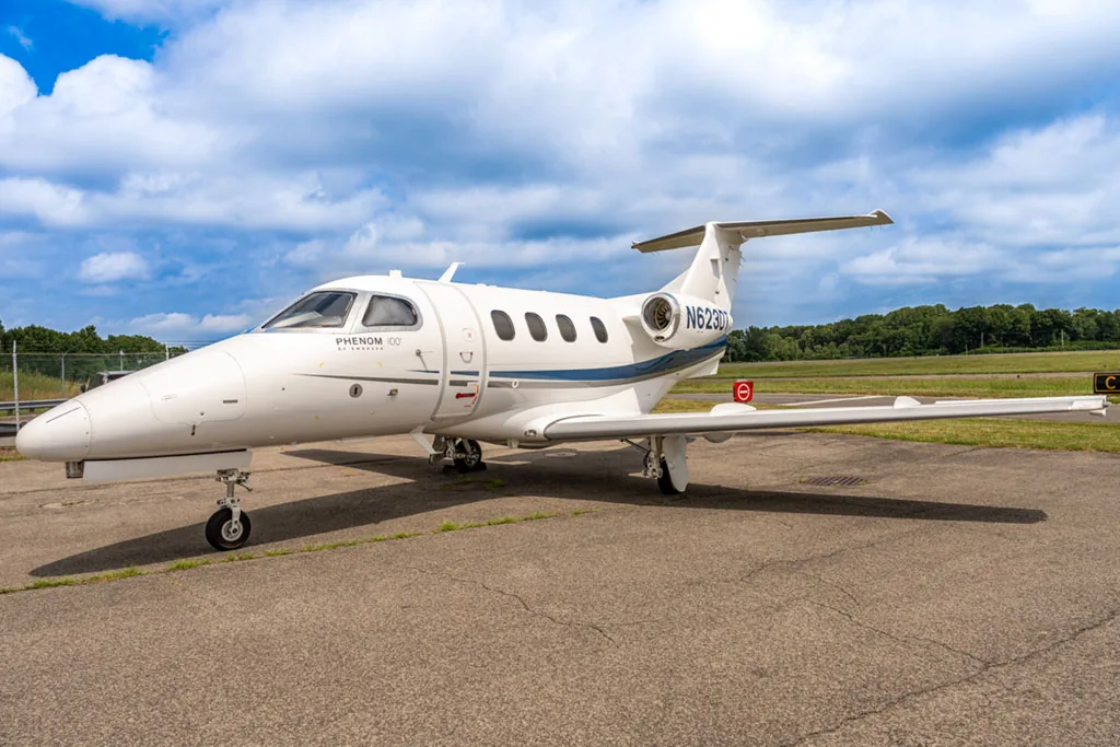 A side view of a white Embraer Phenom 100 business jet with blue and grey stripes, registration N623DT, parked on an airfield.