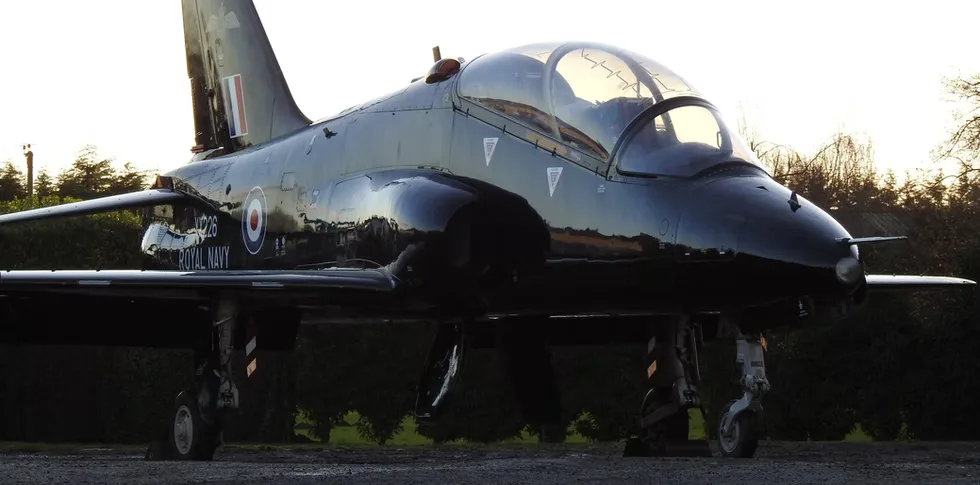 Side view of a black Royal Navy BAE Hawk jet aircraft parked on the ground at sunset.
