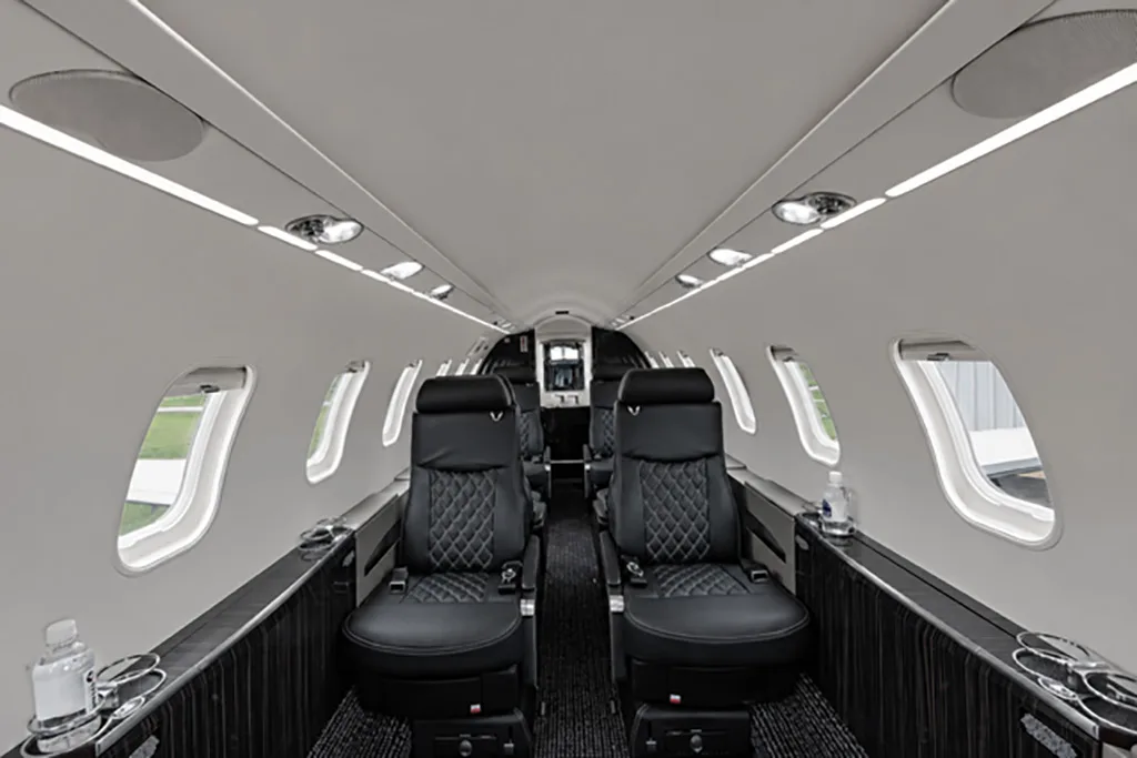 The luxurious interior cabin of a private jet with black quilted leather seats and dark wood accents.