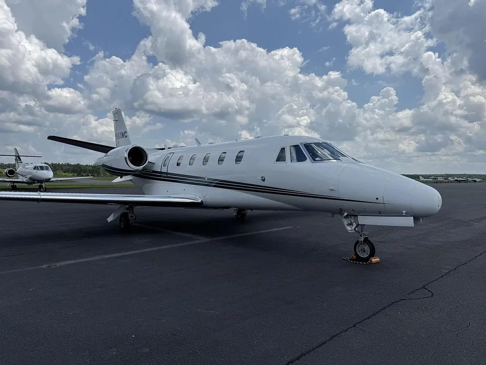 A side view of a white Cessna Citation private jet with black and grey stripes parked on an airport tarmac.