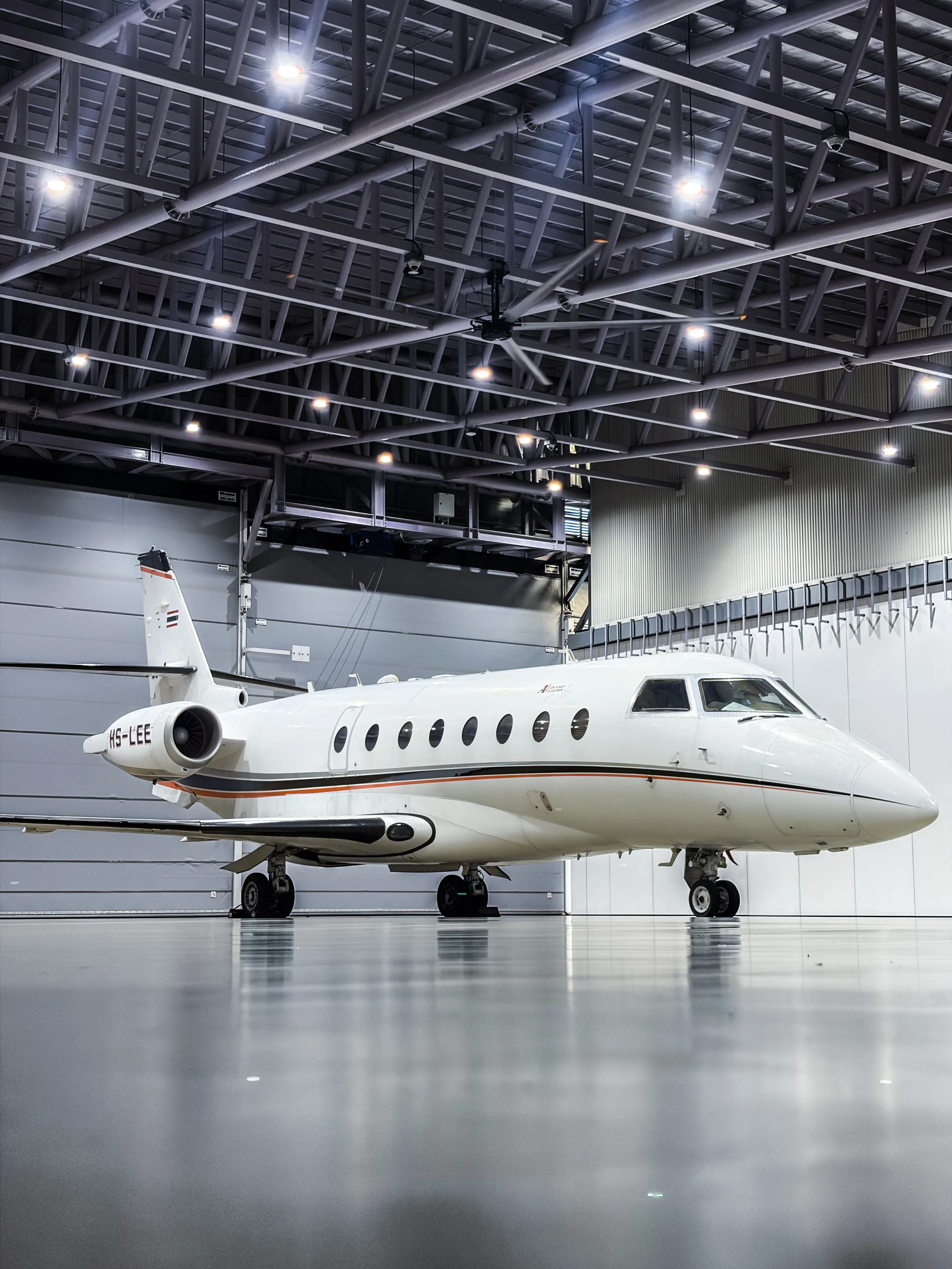 Side view of a white aircraft with orange and black stripes parked inside a hangar.
