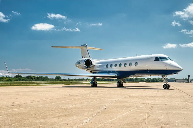 A white Gulfstream G550 business jet with blue and gold stripes parked on the tarmac, viewed from the front-right.