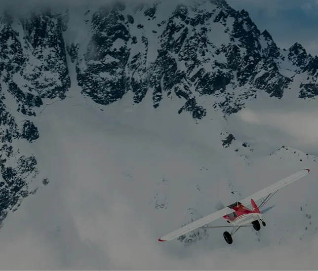 Red and white aircraft flying near a snow-covered mountain.