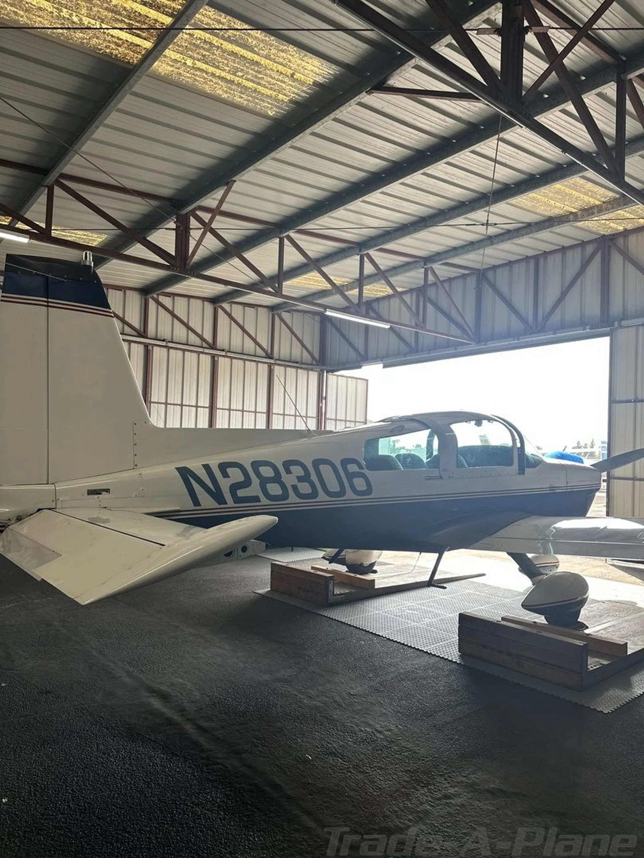 A blue and white Grumman AA5B Tiger aircraft, N28306, parked in a hangar, viewed from the rear left.