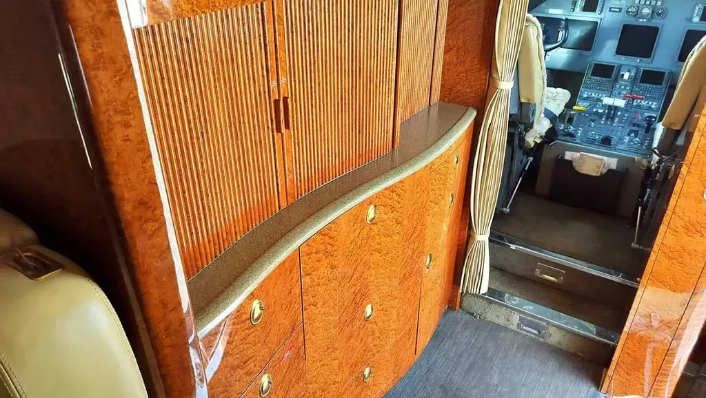 A section of the private jet cabin with polished wood cabinets and drawers, looking towards the cockpit entrance.