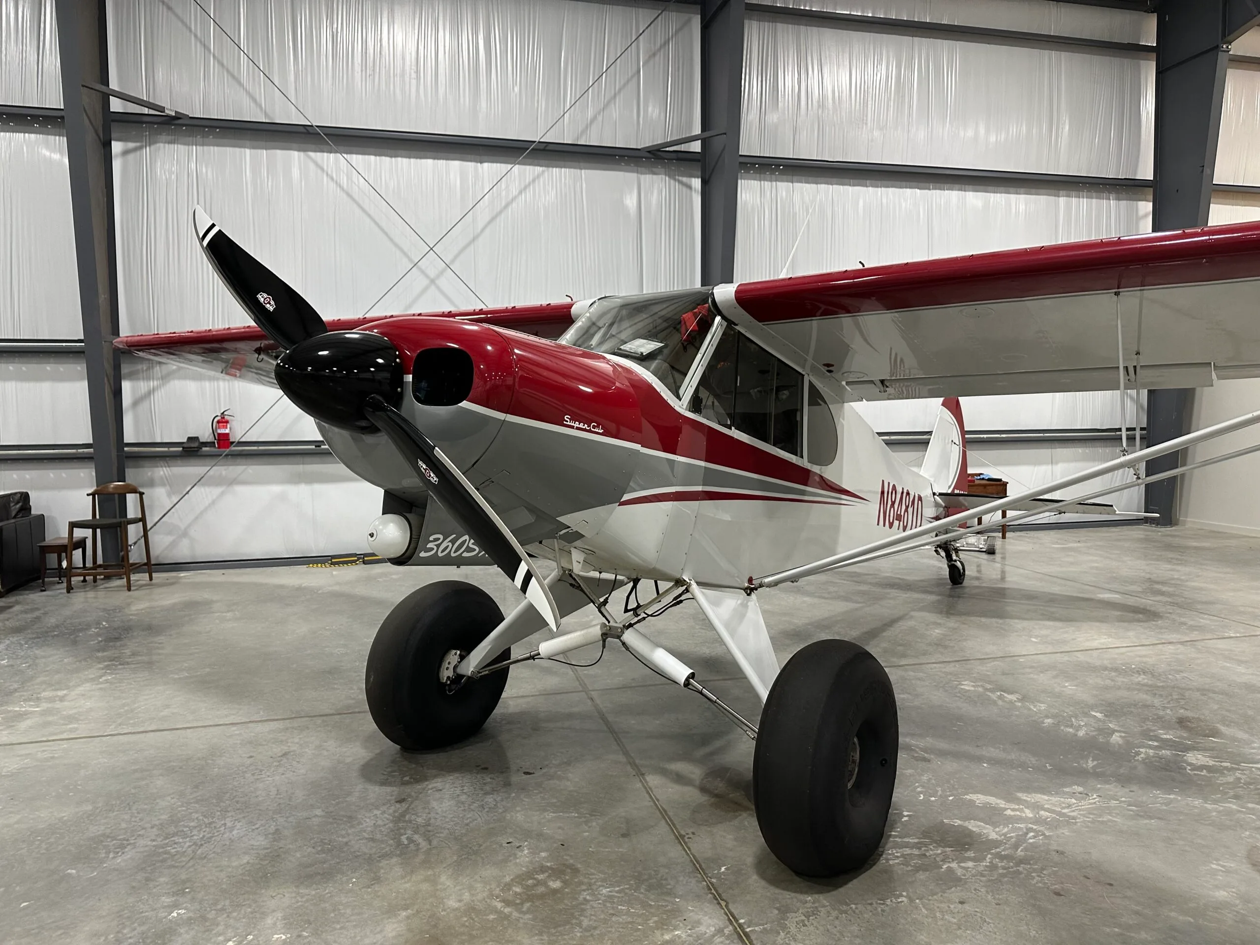 A red, white, and grey Super Cub aircraft with large tundra tires is parked inside a hangar.