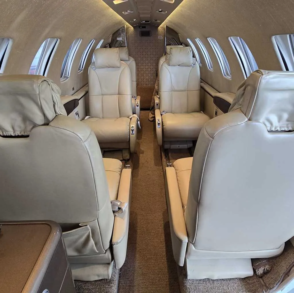 Interior view of a private jet cabin with light beige leather seats and a central aisle.