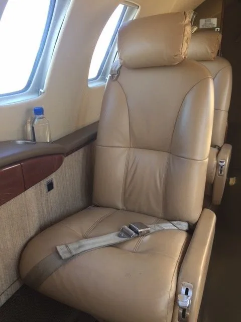 Aircraft interior with a tan leather seat and a bottle of water on the side table.