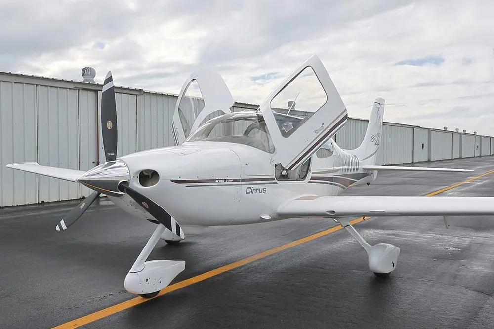 Front-left view of a white Cirrus SR22 aircraft with N3000D registration and both doors open, parked on a wet tarmac.