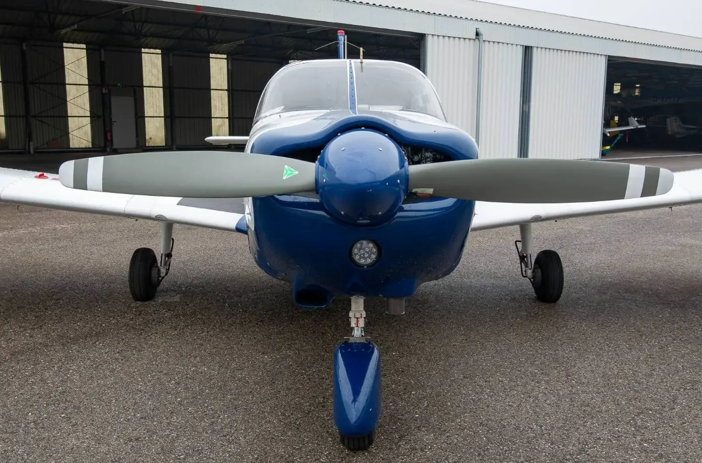 A head-on view of the blue and white single-engine propeller aircraft, showing its propeller and landing gear.