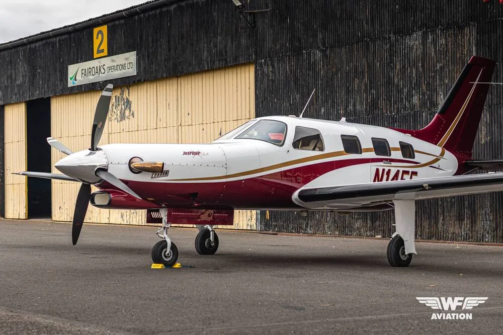 A three-quarter front view of the N14EF turboprop aircraft, white and maroon with gold trim, parked in front of a dark hangar.