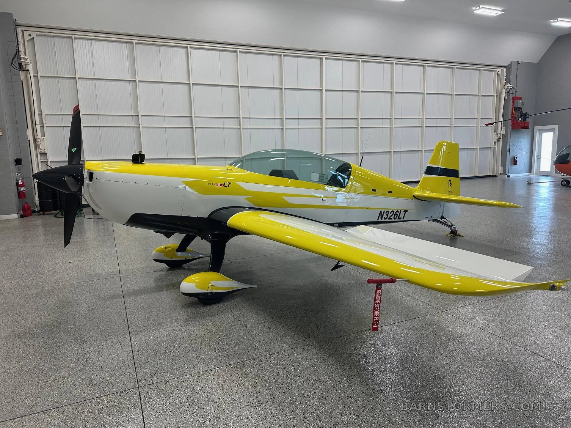 A yellow and white Extra 330LT aerobatic aircraft with registration N326LT, viewed from the front-right in a hangar.