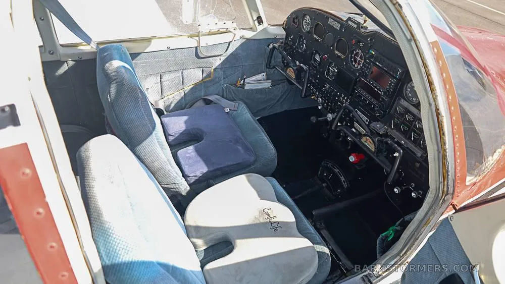 The interior cabin of a small aircraft showing two front seats with cushions and the cockpit beyond.