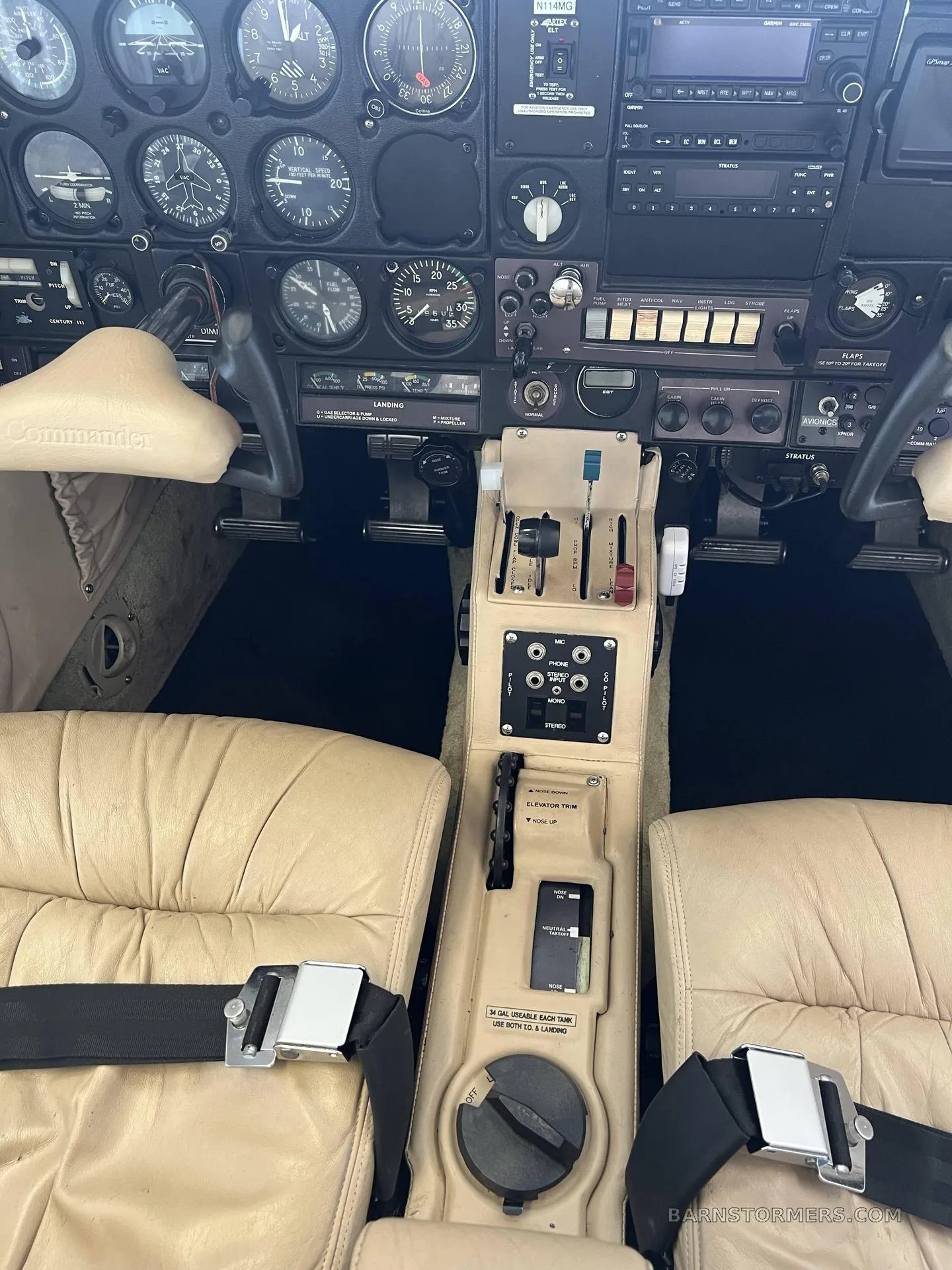 The cockpit of a Commander aircraft with a beige interior, showing the instrument panel, controls, and front seats.