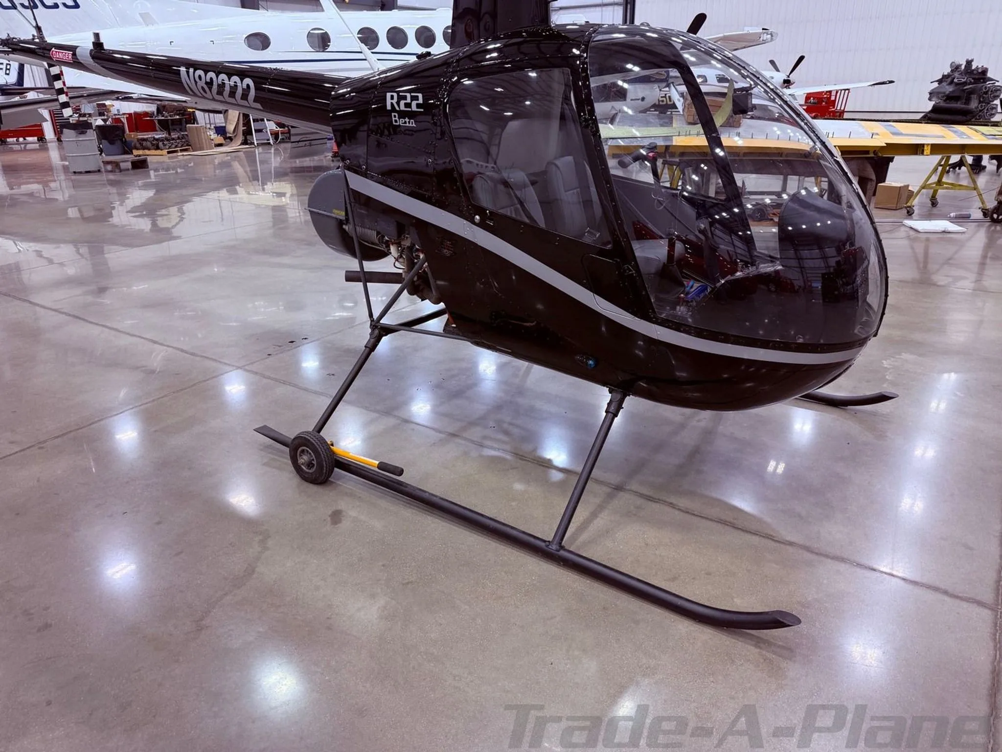 A black Robinson R22 Beta helicopter with a white stripe, registration N82222, parked in a hangar.