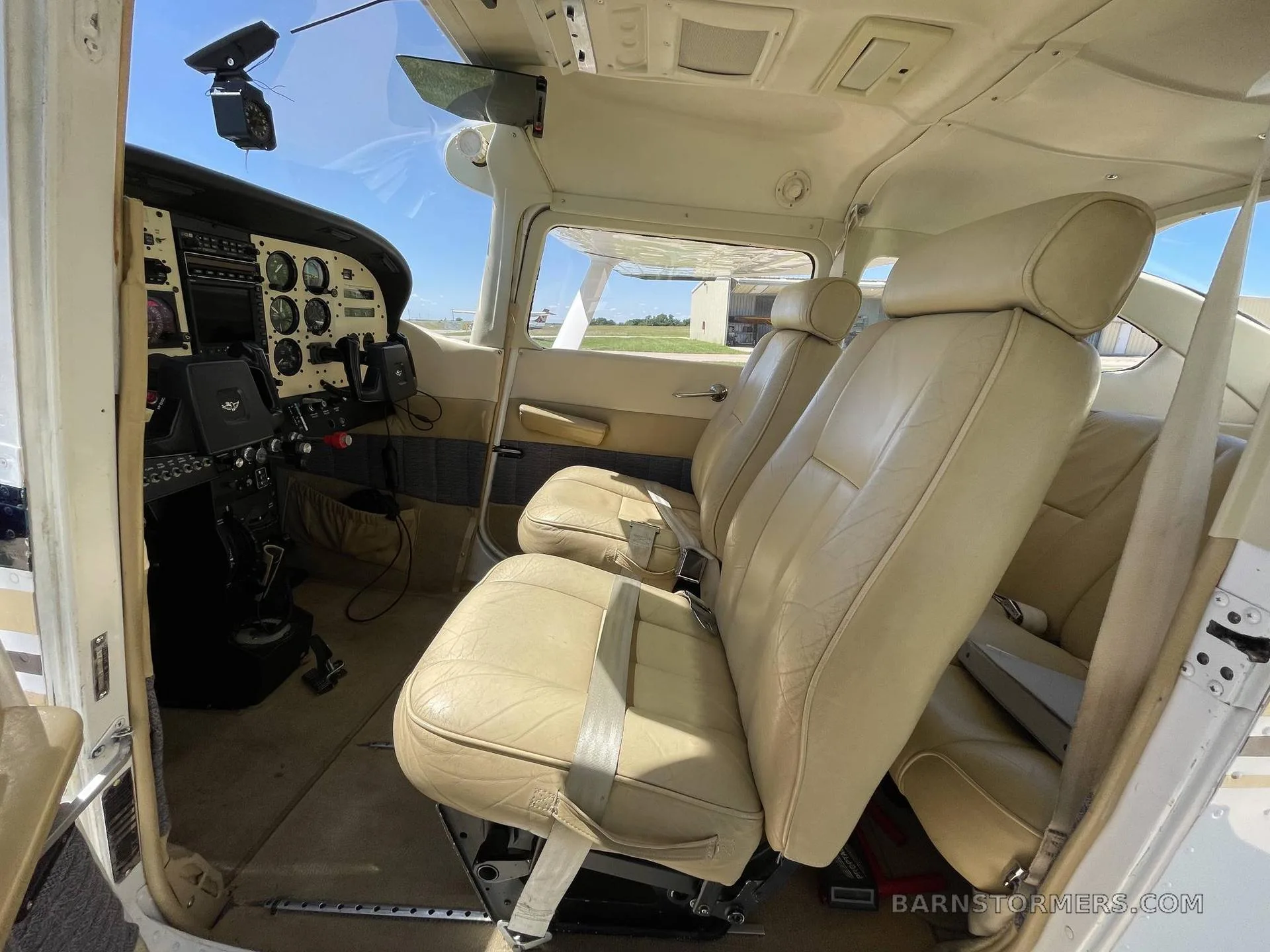 The light tan leather front seats and a partial view of the instrument panel in a small aircraft cabin.