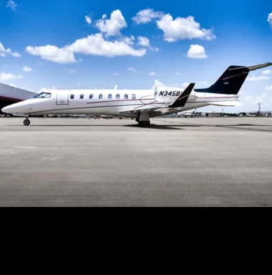A white business jet with a dark blue tail, registration N345B, parked on an airport tarmac under a blue sky.