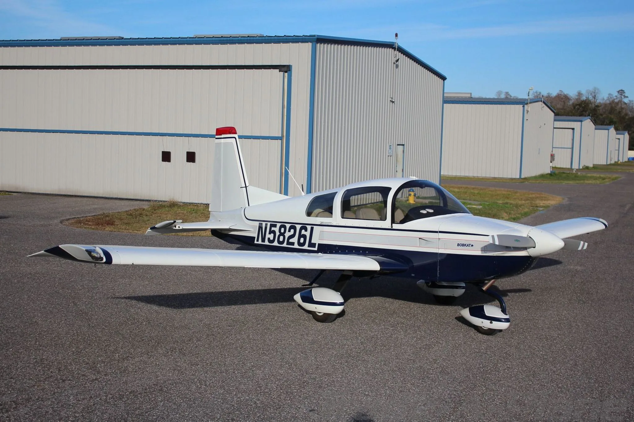 A white and blue Grumman AA-5B Tiger aircraft (N5826L) parked on an airfield, viewed from the front-right.