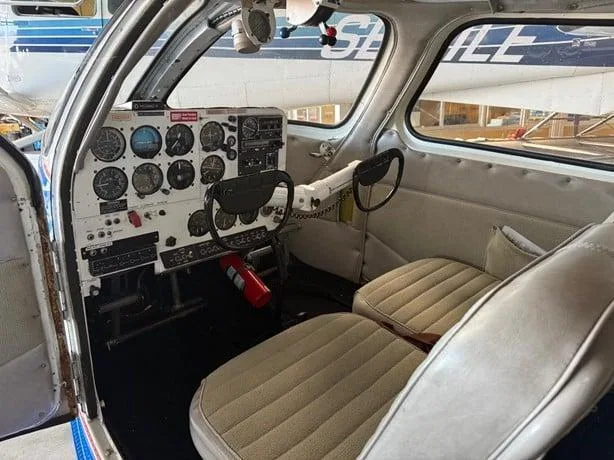 The cockpit interior of an aircraft, showing the instrument panel, dual yokes, and two front seats.