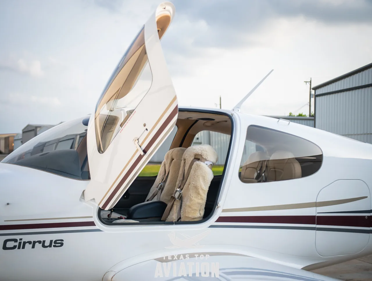 A close-up view of the open passenger door of a white Cirrus SR22 aircraft, revealing sheepskin seat covers inside.