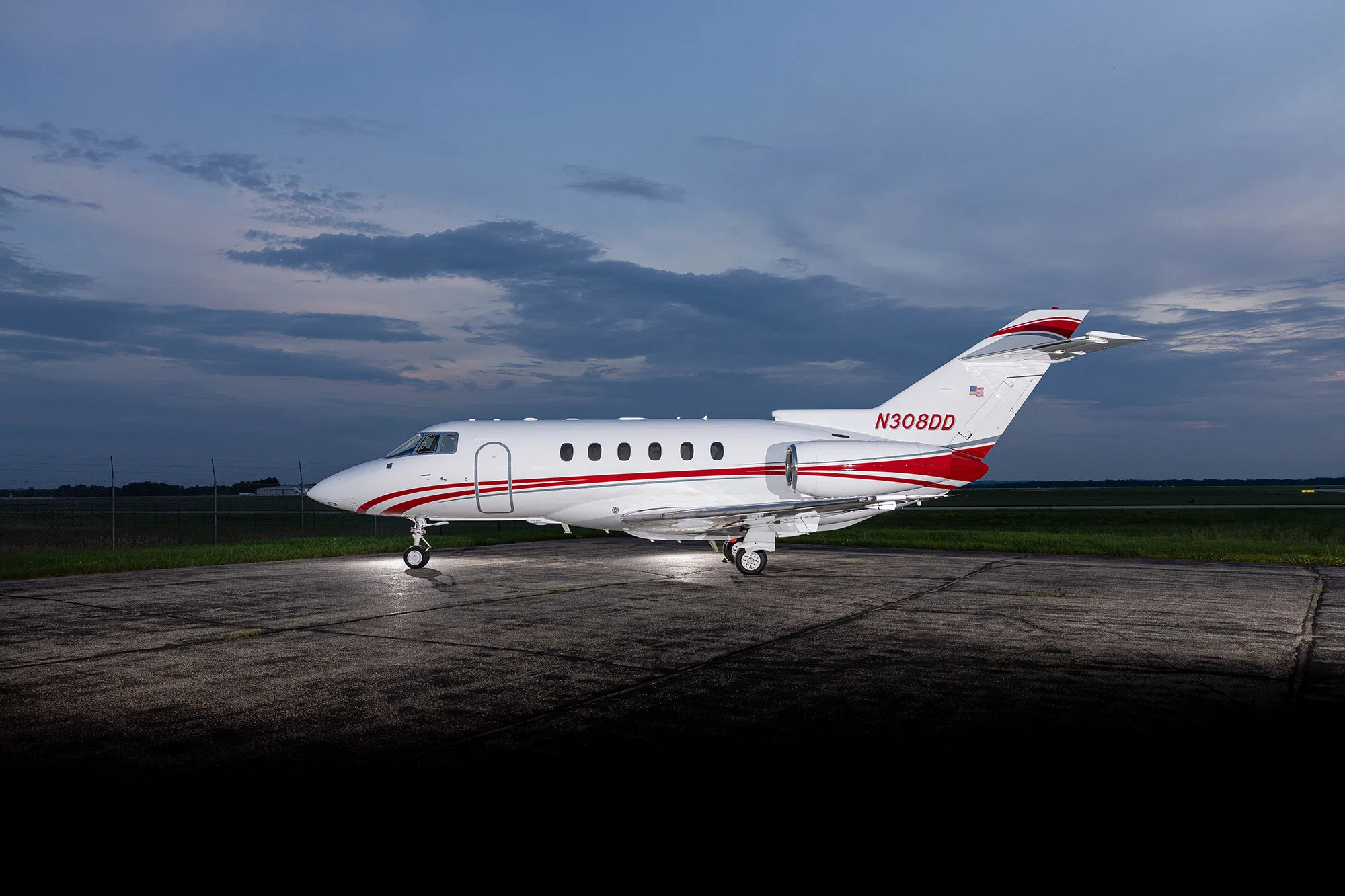 A white business jet with red stripes, registration N308DD, parked on an airfield at dusk, viewed from the side.