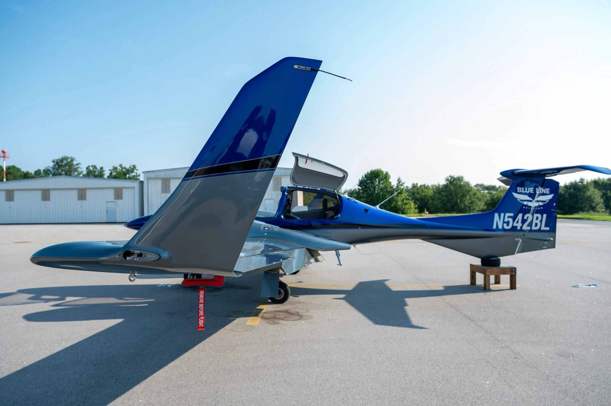 Rear-side view of a blue and grey Diamond DA42 aircraft with doors open, parked on an airfield.