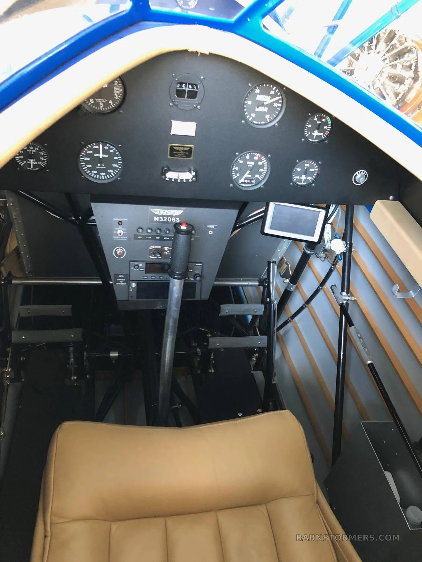 The cockpit of a biplane showing the instrument panel, control stick, and a tan seat.