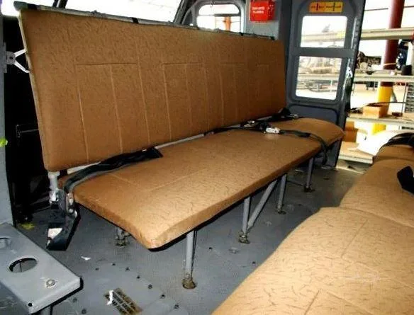The brown bench seats of a helicopter cabin are visible, with a view towards the rear door.