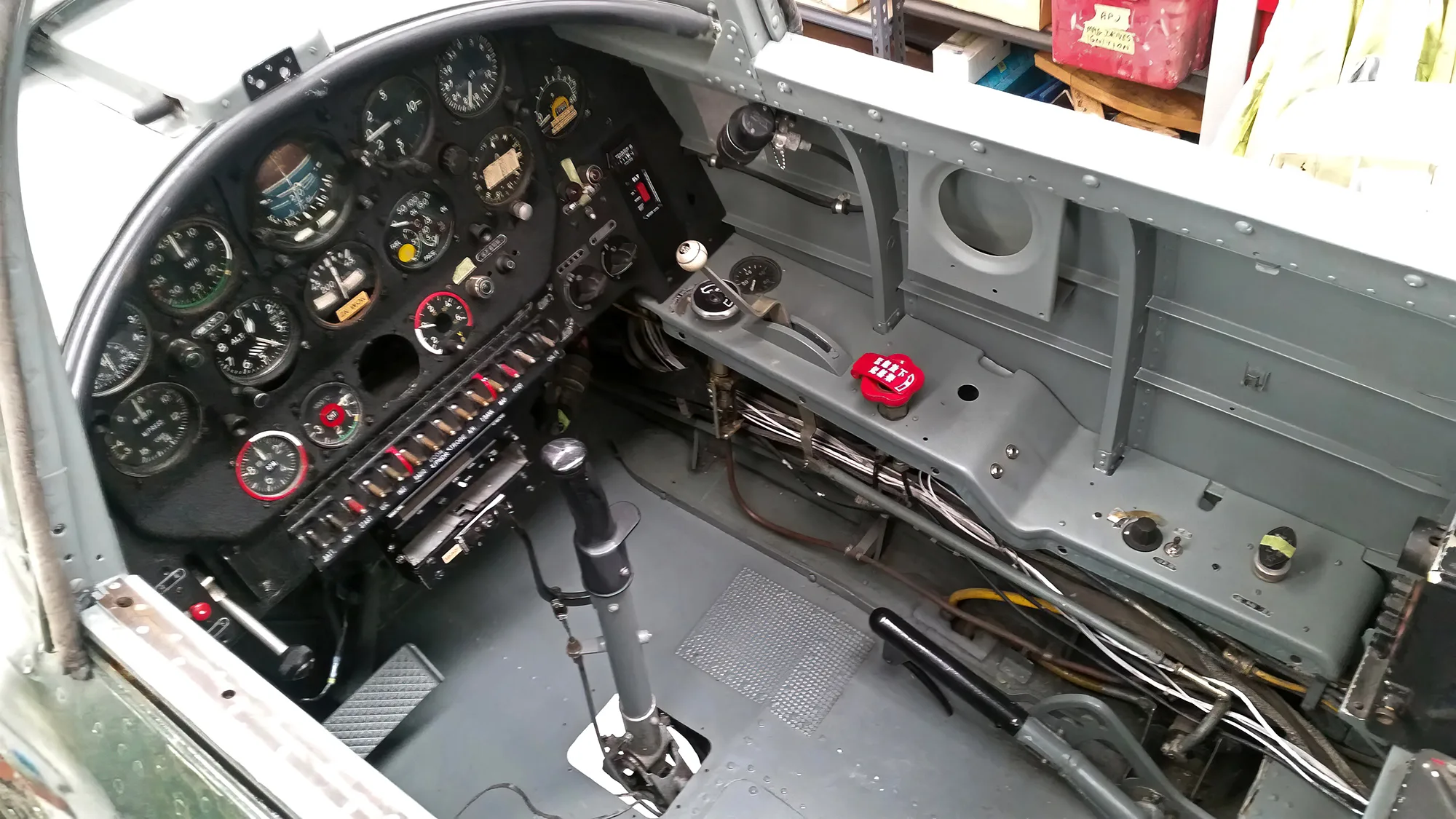 The cockpit of an aircraft showing the instrument panel with many gauges, a control stick, and throttle quadrant.