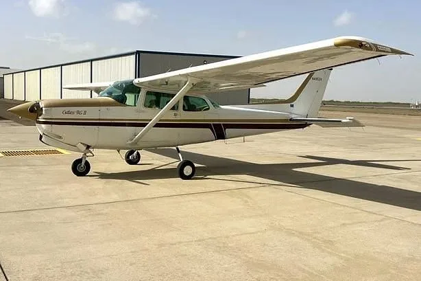 A white and gold Cessna Cutlass RG II (N4953V) parked on a tarmac next to a hangar.