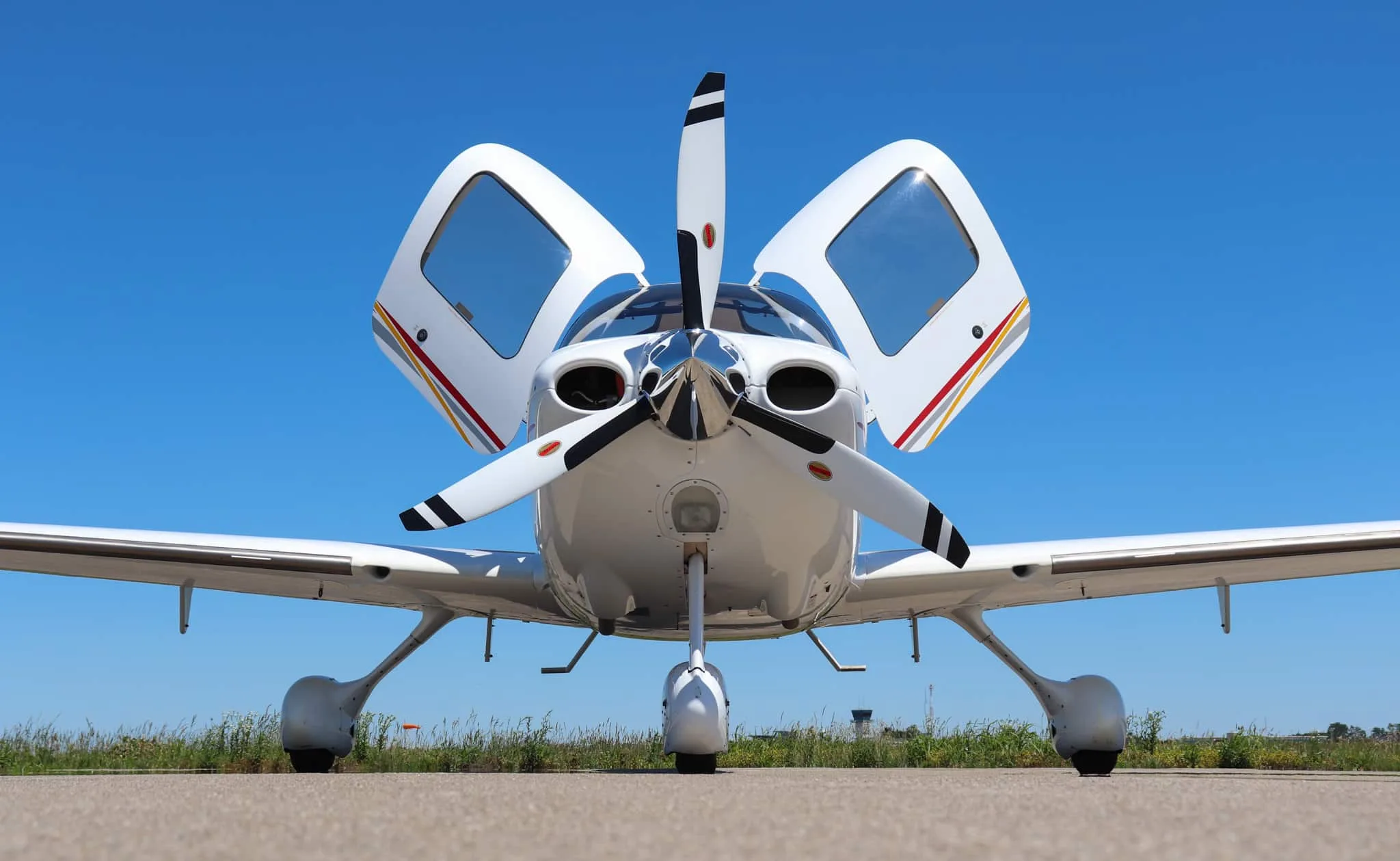 Low-angle head-on view of a white Cirrus SR22 aircraft with open gull-wing doors on a tarmac.