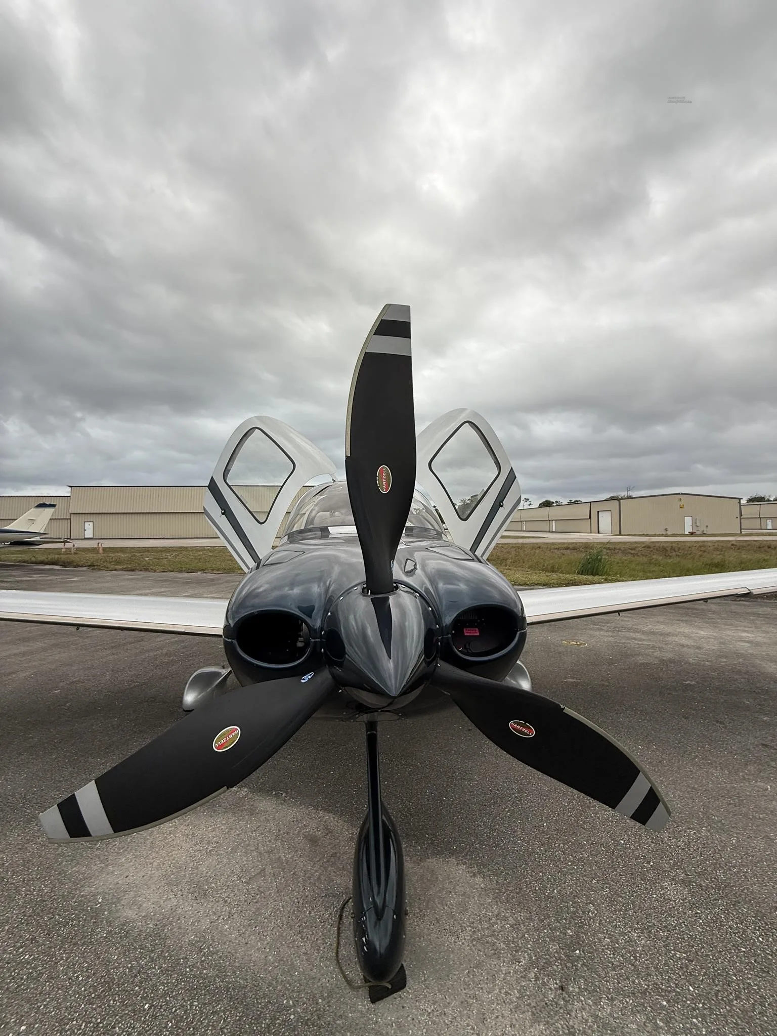A head-on view of the Cirrus SR22T aircraft, N228CC, with its propeller and open gull-wing doors, parked on an airfield.