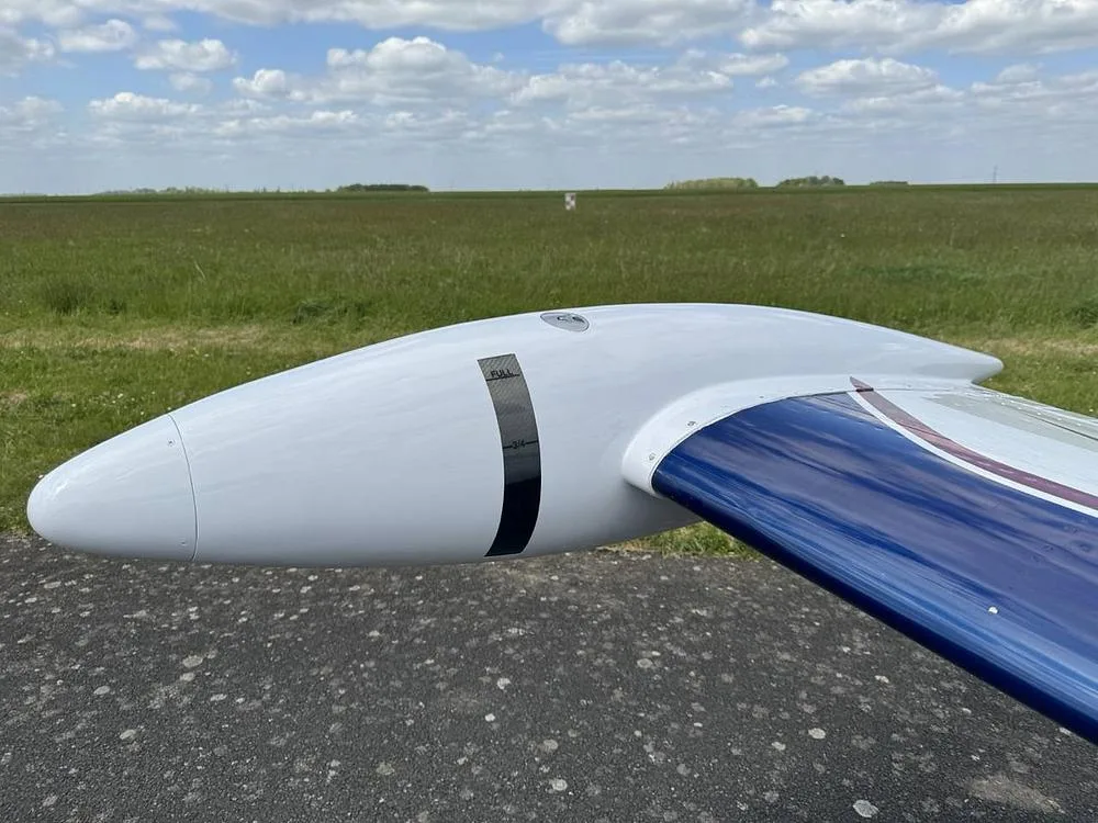 A close-up view of the white wingtip fuel tank with a blue stripe on a Beechcraft Bonanza aircraft.