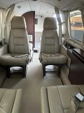 The interior cabin of an aircraft with four beige leather seats and a light-colored carpet.