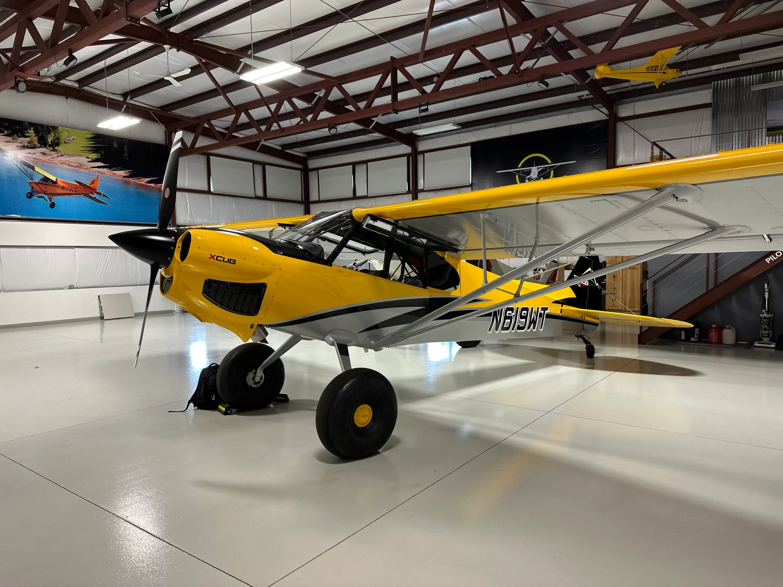 A yellow and grey X-Cub aircraft with registration N619WT is parked inside a well-lit hangar.