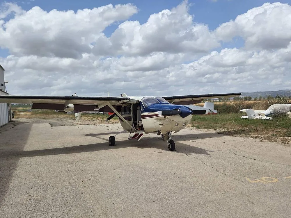 A cream, blue, and maroon Cessna 337 Skymaster with its door open, parked on an airfield under a cloudy sky.