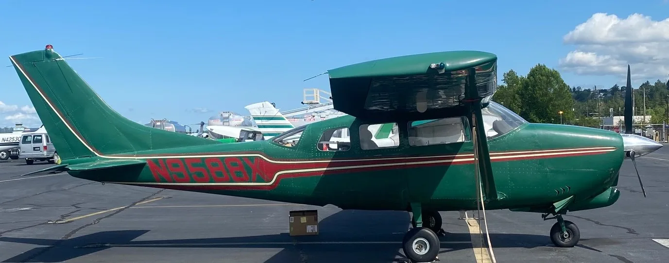 A green Cessna 210 aircraft with red and white stripes parked on an airfield.