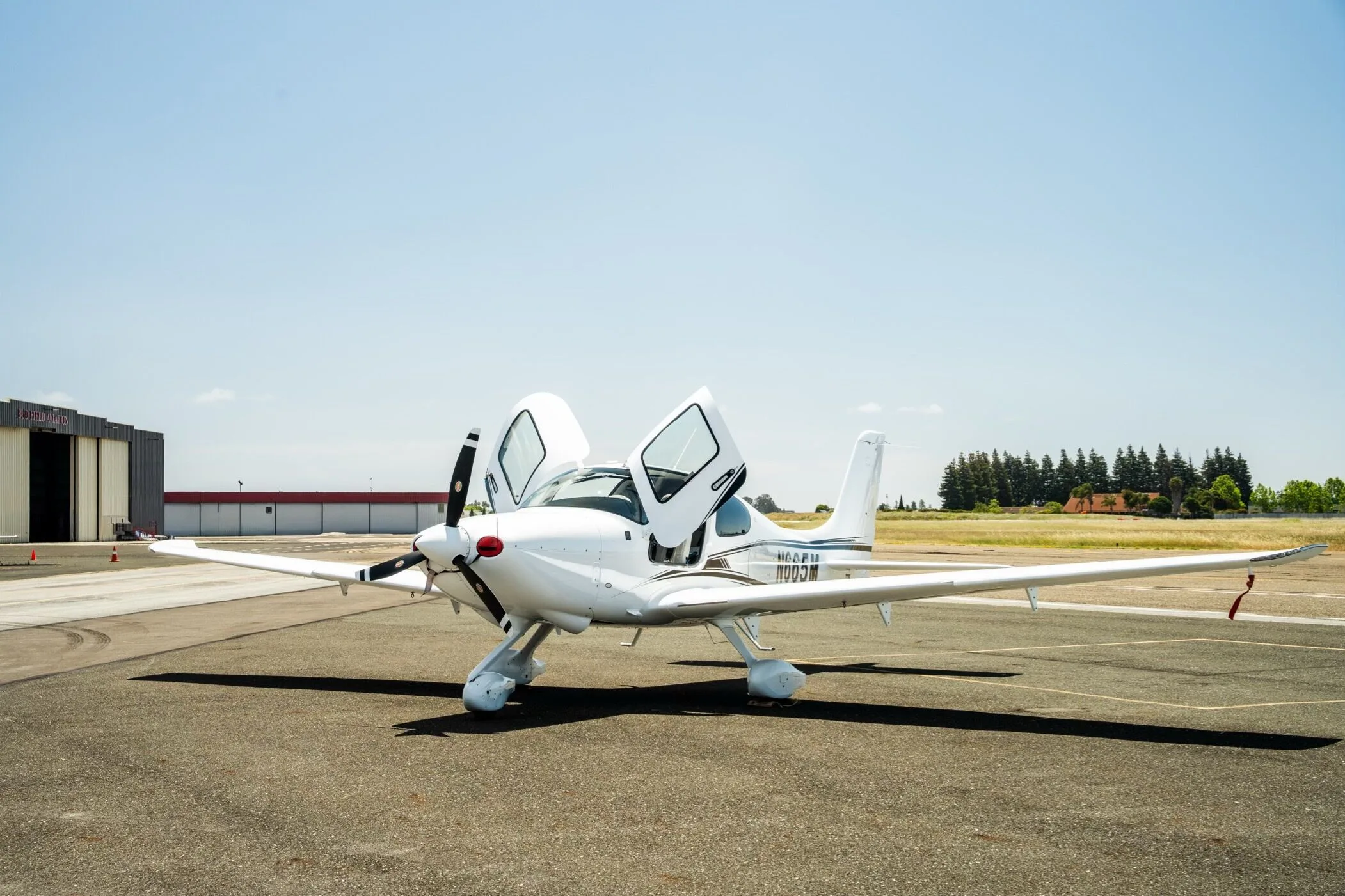 A white Cirrus SR22 aircraft with registration N665M parked on the tarmac with both doors open, viewed from the front.