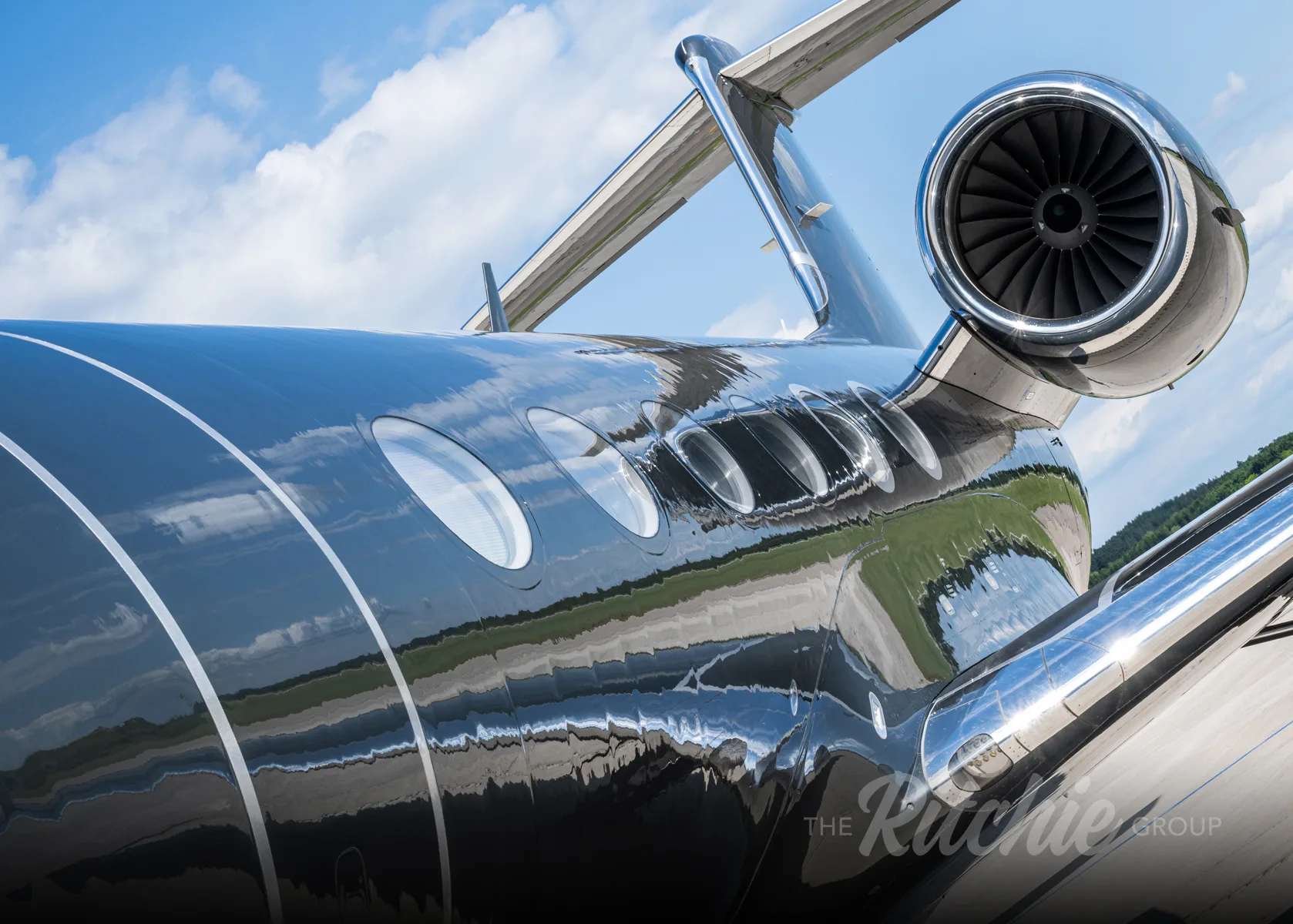 A close-up view of the rear fuselage and engine of a dark grey Gulfstream G650 business jet, showing reflections.
