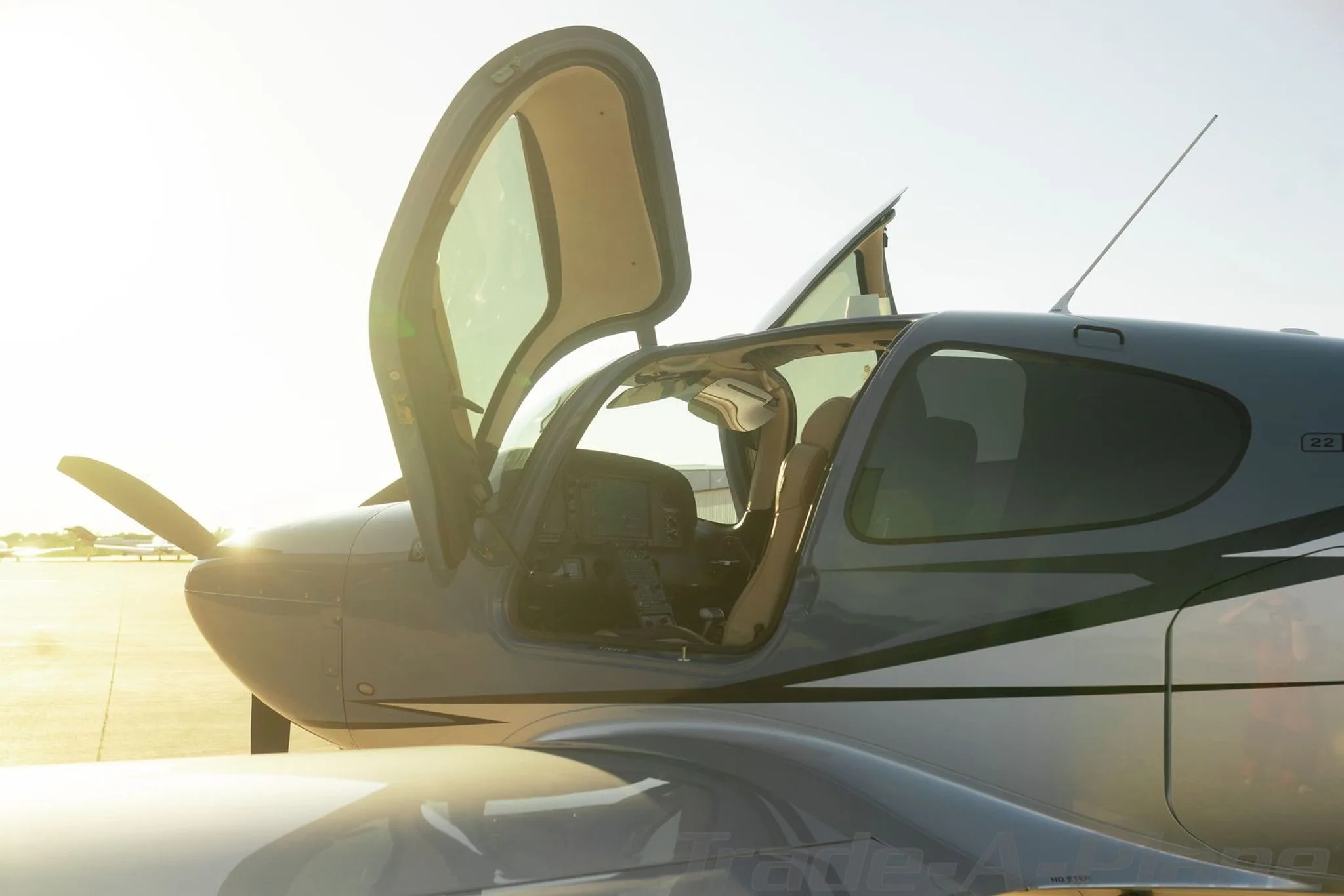 A close-up side view of a grey Cirrus SR22 aircraft with both gull-wing doors open, showing the interior and cockpit.