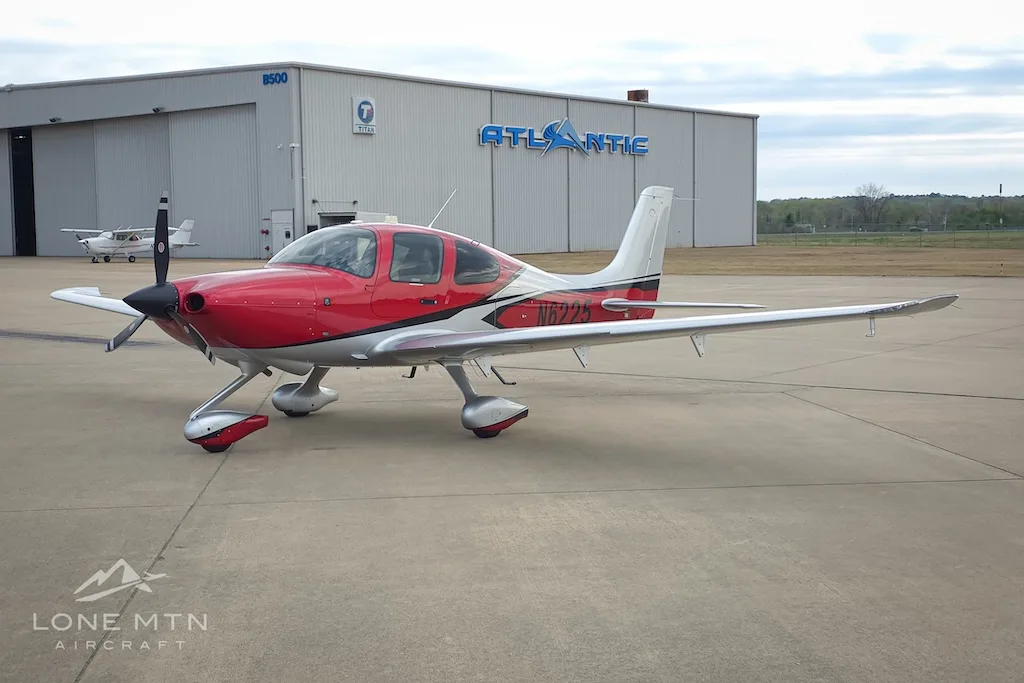 A red and silver Cirrus SR22 aircraft, N6225, parked on an airport apron in front of an Atlantic Aviation hangar.