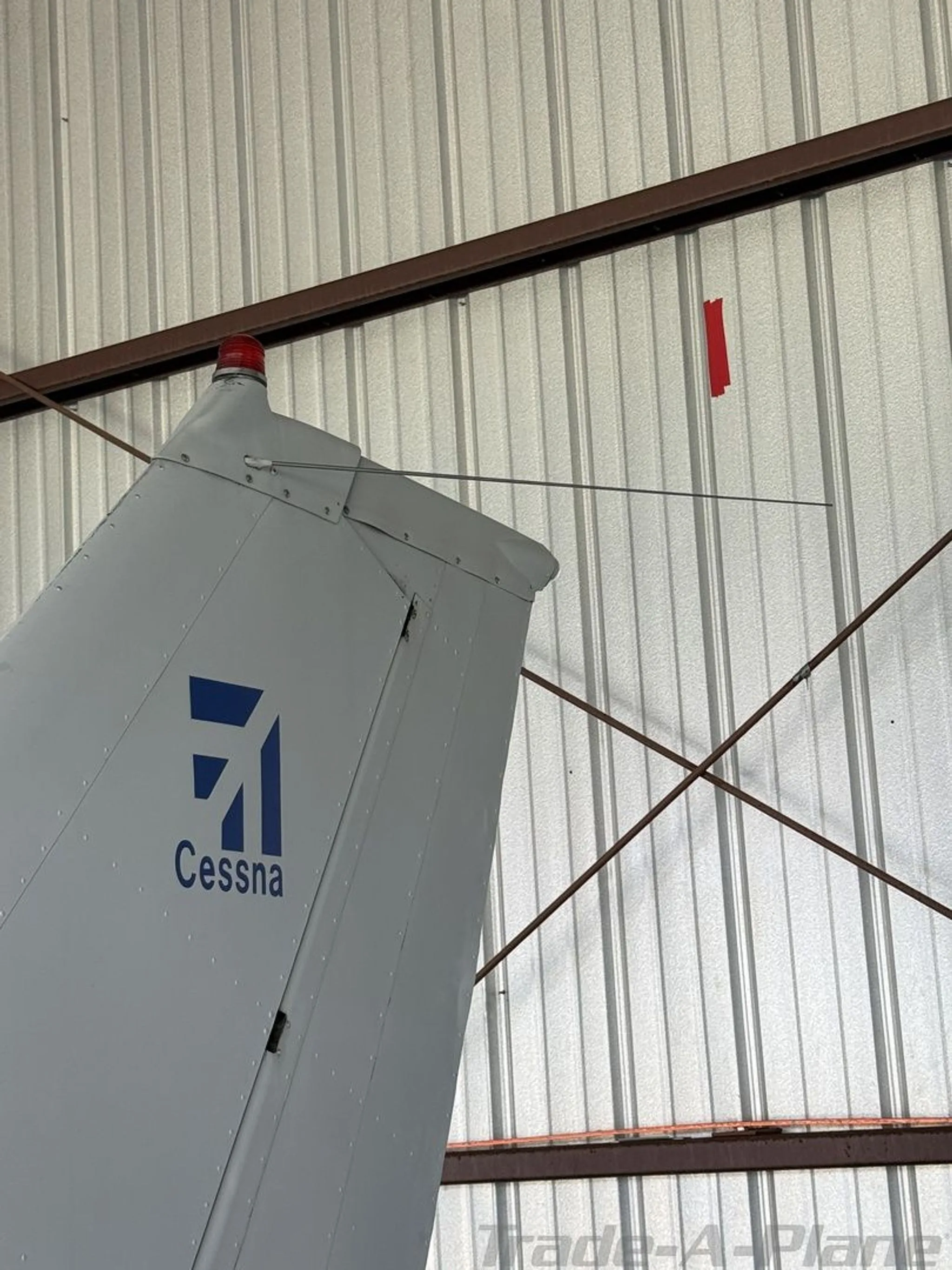 A close-up of the Cessna Skyhawk's white tail with the blue Cessna logo and a red beacon light.