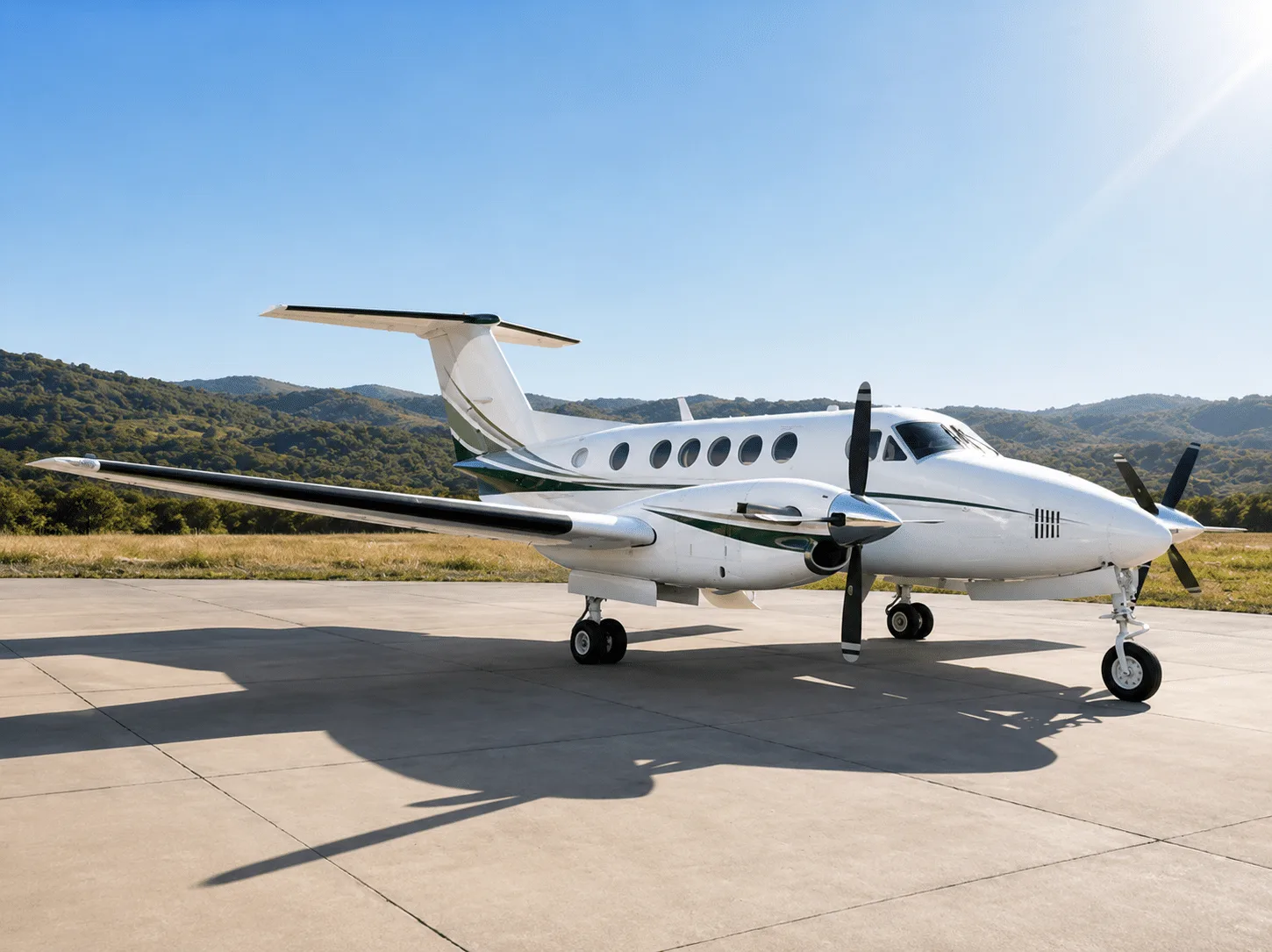 A white twin-turboprop aircraft with green and black stripes is parked on a concrete tarmac under a clear blue sky with hills in the background.
