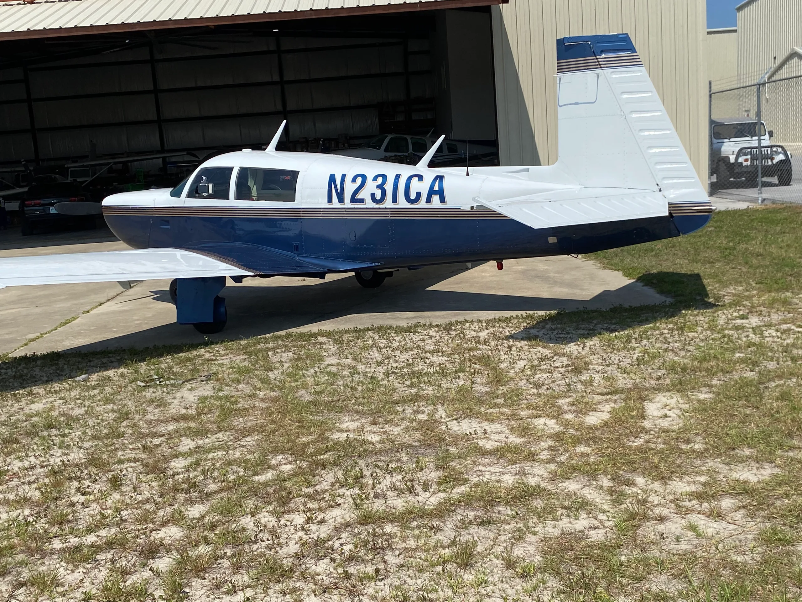 Side view of a blue and white single-engine aircraft (N231CA) parked in front of an open hangar.