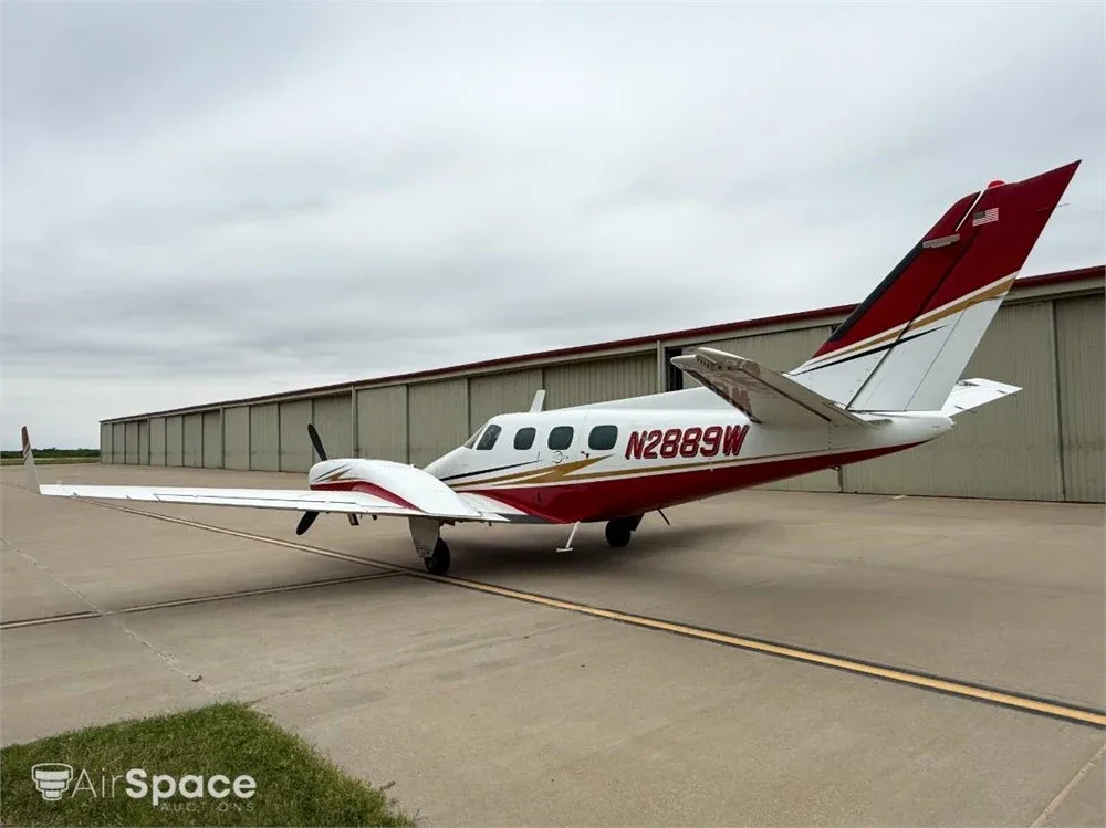 A white and red Beechcraft Duke N2889W parked on a tarmac next to a hangar under a cloudy sky.