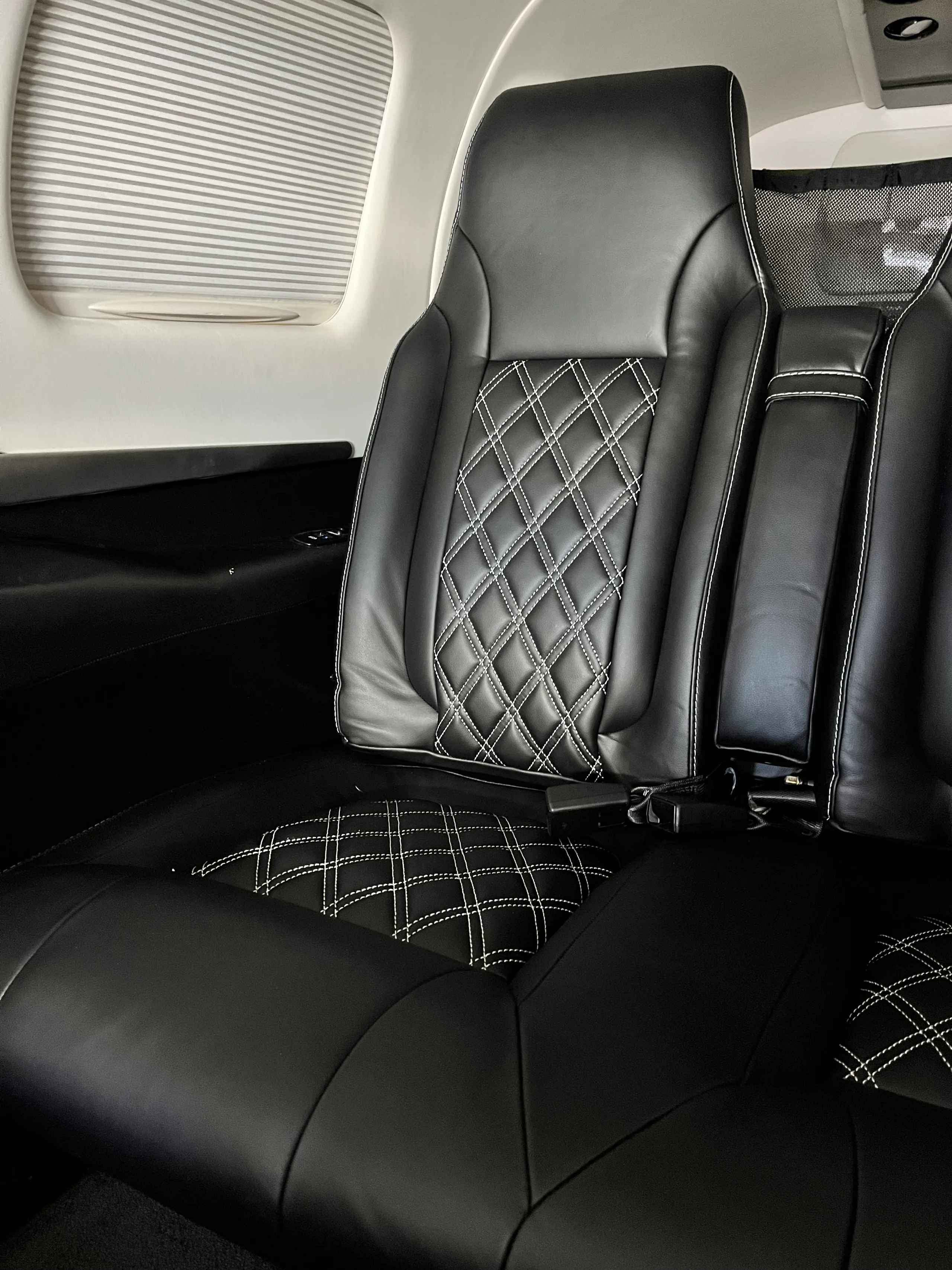 A close-up view of a black leather aircraft cabin seat with white diamond stitching.