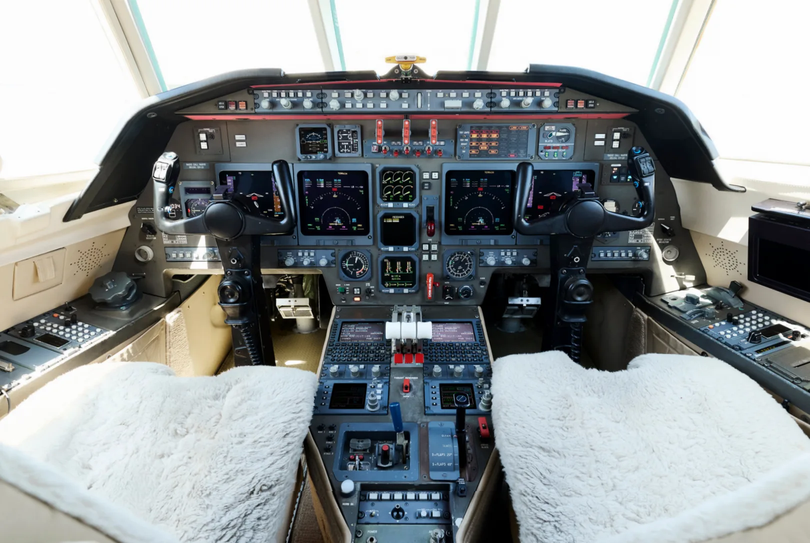 The cockpit of a business jet features multiple digital displays, control yokes, and a central throttle quadrant.